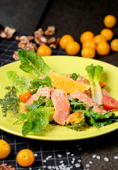 Cold salmon salad with green leaves, cucumber, avocado, lime and tomato on black stone background. Top view with copy space. Rustic style.