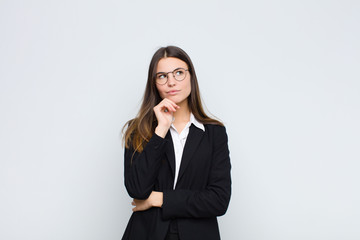 young businesswoman feeling thoughtful, wondering or imagining ideas, daydreaming and looking up to...