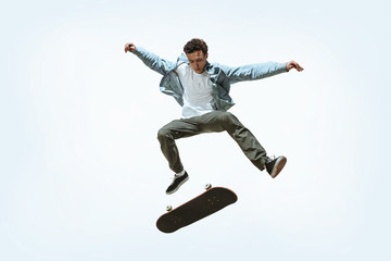 Caucasian young skateboarder riding isolated on a white studio background. Man in casual clothing training, jumping, practicing in motion. Concept of hobby, healthy lifestyle, youth, action, movement. © master1305
