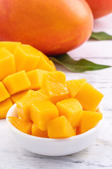 Fresh mango,beautiful chopped fruit with green leaves on bright wooden table background. Tropical fruit design concept, close up, copy space.