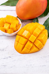 Fresh mango,beautiful chopped fruit with green leaves on bright wooden table background. Tropical...