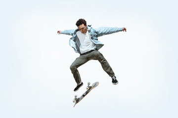 Caucasian young skateboarder riding isolated on a white studio background. Man in casual clothing training, jumping, practicing in motion. Concept of hobby, healthy lifestyle, youth, action, movement.