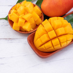 Fresh mango,beautiful chopped fruit with green leaves on bright wooden table background. Tropical fruit design concept, close up, copy space.