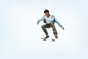 Obraz na płótnie Canvas Caucasian young skateboarder riding isolated on a white studio background. Man in casual clothing training, jumping, practicing in motion. Concept of hobby, healthy lifestyle, youth, action, movement.
