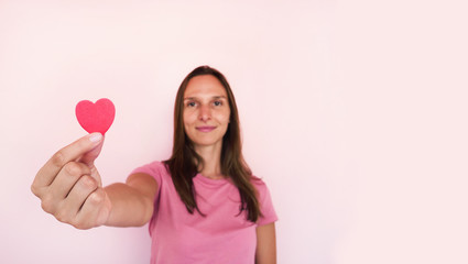 Obraz na płótnie Canvas Girl shows to camera heart shape at pink wall at background. Valentines day concept banner