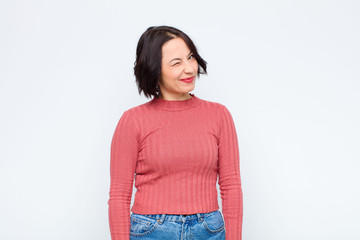 young pretty woman looking happy and friendly, smiling and winking an eye at you with a positive...