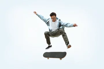 Fotobehang Caucasian young skateboarder riding isolated on a white studio background. Man in casual clothing training, jumping, practicing in motion. Concept of hobby, healthy lifestyle, youth, action, movement. © master1305