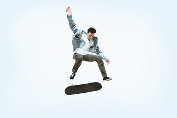 Caucasian young skateboarder riding isolated on a white studio background. Man in casual clothing training, jumping, practicing in motion. Concept of hobby, healthy lifestyle, youth, action, movement.