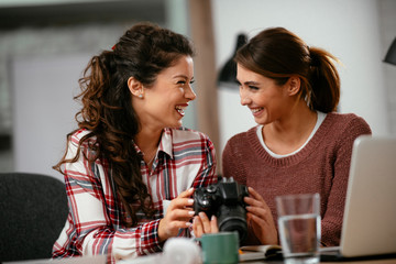 Young woman showing colleague pictures in camera. Two beautiful businesswomen having fun in office. 