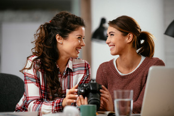 Young woman showing colleague pictures in camera. Two beautiful businesswomen having fun in office. 