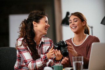 Young woman showing colleague pictures in camera. Two beautiful businesswomen having fun in office. 