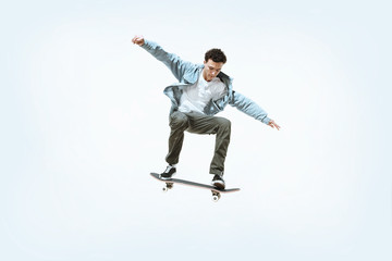 Naklejka na ściany i meble Caucasian young skateboarder riding isolated on a white studio background. Man in casual clothing training, jumping, practicing in motion. Concept of hobby, healthy lifestyle, youth, action, movement.