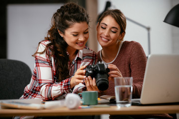 Young woman showing colleague pictures in camera. Two beautiful businesswomen having fun in office. 
