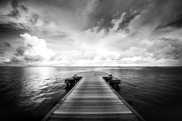 Idyllic or dramatic bungalow on water, Maldive Islands. Dramatic black and white process for loneliness or inspiration. Perspective view at sea from center of wooden pier dramatic sky at daylight.
