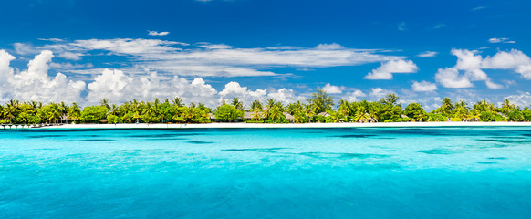 Maldives island panorama. Summer beach landscape, fantastic blue sky palm trees over white sandy beach, villas in luxury resort or hotel. Summer vacation scenery