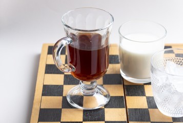 Cup of coffee, glass of milk, bowl with ice on chess board