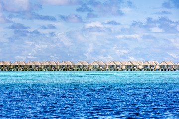 Luxury water villas in Maldives fantastic blue sea. Seascape and endless horizon under blue sky with clouds. Tropical nature pattern