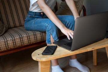 Woman is sitting on a sofa and using a laptop at wooden table. Study and work online, freelance....