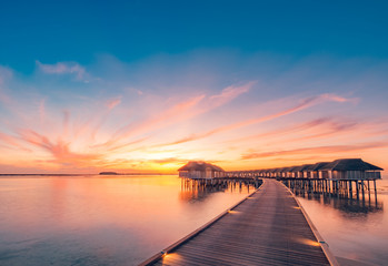 Fototapeta na wymiar Sunset on Maldives island, luxury water villas resort and wooden pier. Beautiful sky and clouds and beach background for summer vacation holiday and travel concept