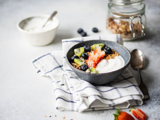 Delicious healthy breakfast - granola with yogurt and berries, yogurt in bowl and granola in glass jar on the table. Copy space.