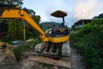 The modern excavator on the construction site with sunset sky. Large tracked excavator standing on a hill with a green grass. Machinery for a construction of a new building in the countryside.