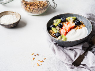 Delicious breakfast - granola with yogurt and berries, dry coconut in bowl and granola in glass jar on the table. Copy space.