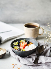 Delicious breakfast - the cup of coffee, dry coconut in bowl, granola with yogurt and berries and open magazine on the table. Copy space.