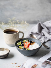 Delicious breakfast - the cup of coffee, dry coconut in bowl, granola with yogurt and berries and open magazine on the table. Copy space.