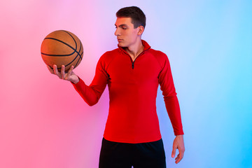 Young athletic man, with basketball, posing on background with neon lights