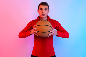 Young athletic man, with basketball, posing on background with neon lights