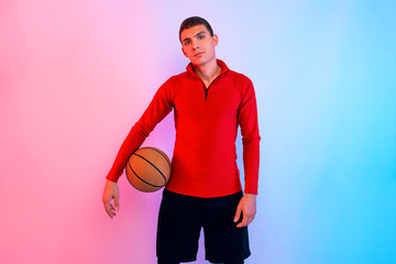 Young athletic man, with basketball, posing on background with neon lights