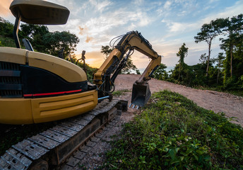 The modern excavator on the construction site with sunset sky. Large tracked excavator standing on a hill with a green grass. Machinery for a construction of a new building in the countryside.