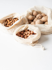 Reusable eco-friendly fabric bags for storage or shopping with various nuts on a white background. Copy space
