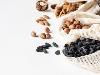 Obraz premium Reusable eco-friendly fabric bags for storage or shopping with various nuts and raisins on a white background. Copy space