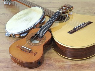 An acoustic guitar and two Brazilian musical instruments: cavaquinho and pandeiro (tambourine), on a wooden surface. The instruments are widely used to accompany samba and choro music. - obrazy, fototapety, plakaty