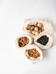 Reusable eco-friendly fabric bags for storage or shopping with various nuts and raisins on a white background.
