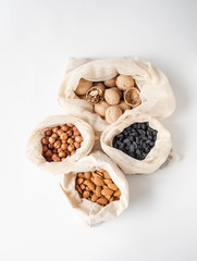 Reusable eco-friendly fabric bags for storage or shopping with various nuts and raisins on a white background.
