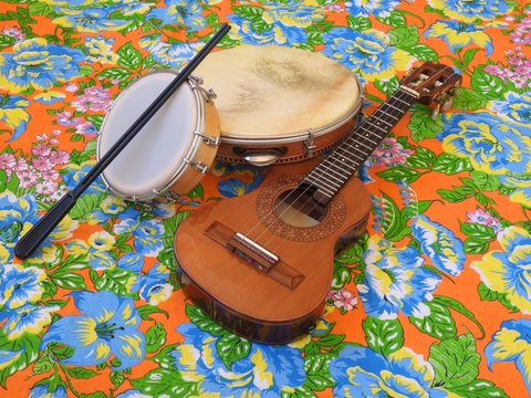 Three Brazilian musical instruments: cavaquinho, pandeiro (tambourine) and tamborim with drumstick on a colorful &ldquo;chitao&rdquo; fabric with floral prints. They are widely used in samba and pagode ensembles.