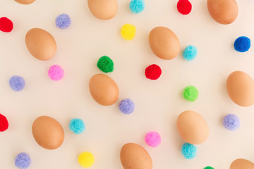 Easter eggs pattern with colorful pompons on beige background.