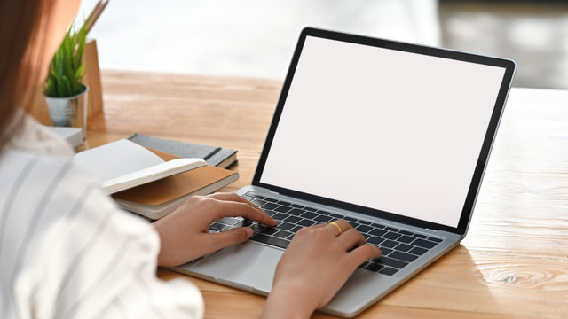 Close-up image of beautiful business woman sitting at the wooden work desk and typing on the white blank screen laptop keyboard.