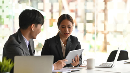 Photo of young confident business woman explaining a new project to her colleague next to her while sitting in the meeting room at the modern office.