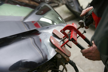 mechanic's hands straighten the car body part. mechanic is aligning car body part