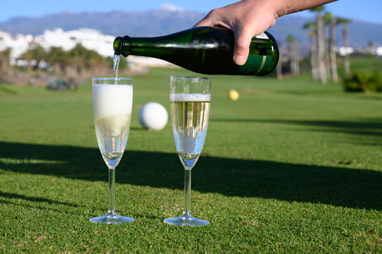 Pouring of bubbles white champagne or cava wine during golf competition event or celebration on green golf club grass with mountains view