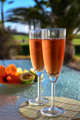 Two glasses of rose bubbles champagne or cava wine served outside on paradise island with palms and green grass