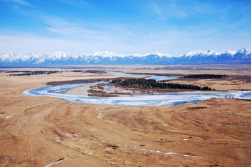 frozen river in the steppe against the backdrop of snowy mountains