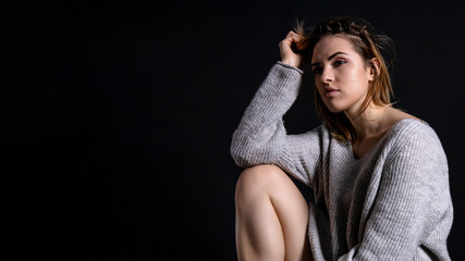 young beautiful girl in a gray sweater with a calm pensive facial expression sits on a dark background, copy space