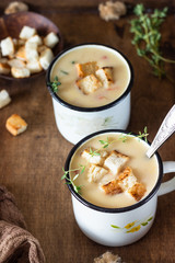 Homemade corn chowder soup with potatoes, carrots, red bell pepper and croutons in white enamel mugs, wooden tray. Delicious cozy first course, comfort food.