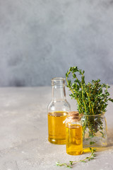 Bottle of thyme (thymus) essential oil with fresh thyme, light grey stone background.