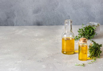 Bottle of thyme (thymus) essential oil with fresh thyme, light grey stone background.