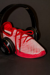 On black background, red sneakers with large black headphones to listen to music when running. Sport. Street style and fashion. Advertizing of footwear.